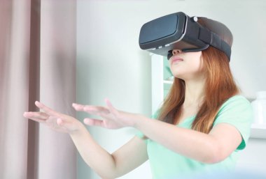 Evde sanal gerçeklik gözlüklü genç kadın. Bir sanal gerçeklik kulaklık takan için sanal gerçeklik sağlar başa takılan bir aygıt olduğunu.