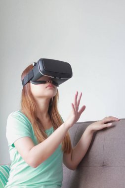 Evde sanal gerçeklik gözlüklü genç kadın.