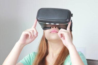 Evde sanal gerçeklik gözlüklü genç kadın.