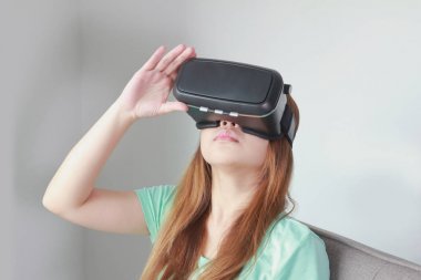 Evde sanal gerçeklik gözlüklü genç kadın.