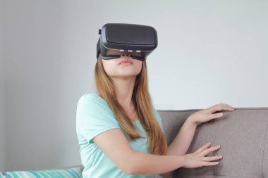 Evde sanal gerçeklik gözlüklü genç kadın.