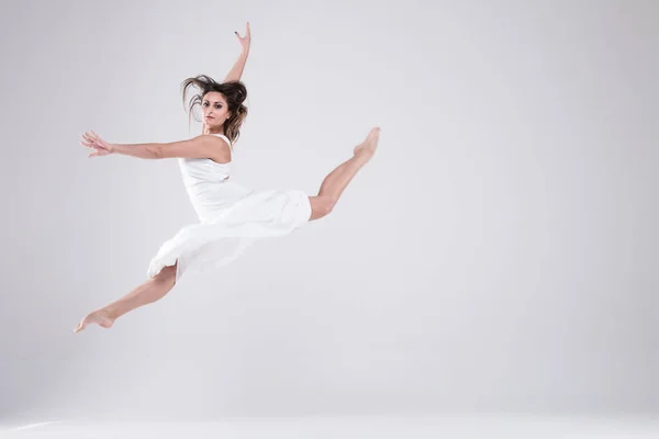 Dancer in jump girl in a white dress, a girl on a light background, brunette in a white dress Portrait of girl in white clothes. Gymnastics, dance, preparation, contemporary, practice, workout, strength, flexibility, stretching, performance.