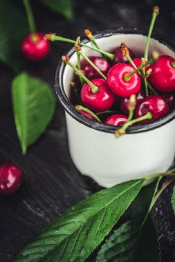 Kiraz koyu ahşap zemin üzerine yeşil yaprakları ile beyaz kupa.