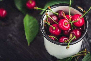 Kiraz koyu ahşap zemin üzerine yeşil yaprakları ile beyaz kupa.