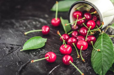 Kiraz koyu ahşap zemin üzerine yeşil yaprakları ile beyaz kupa.