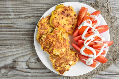 Tavuk göğsü peynir ile kaplı eski ahşap masa üzerinde beyaz tabakta domates