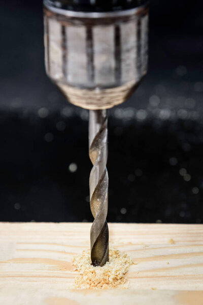 Drilling hole in wood on black background