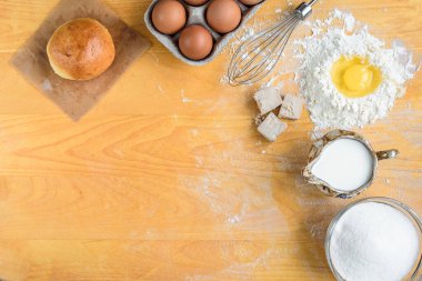 Arkaplan üstü görüntüsü pişiriliyor. Tatlı çörek ya da ekmek hamuru yapmak. Hamur, yumurta, maya, süt, un ile ahşap tahtanın üzerinde hamur işi için malzemeler pişiriyorum..