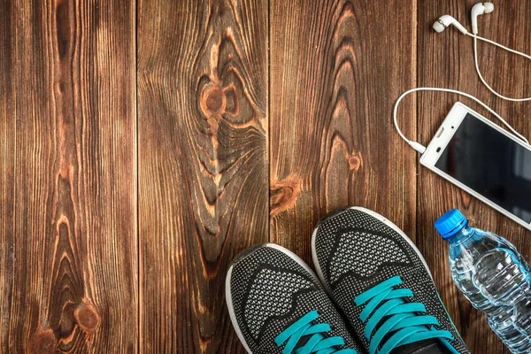 Workout set with sport sneakers, earphones, phone, notebook and drinking water on wood background with copy space. Fitness equipment. Sport concept. Plan for weight loss.