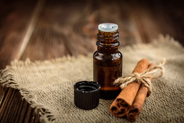Bottle of cinnamon essential oil on dark wooden background. Spa ingredients.