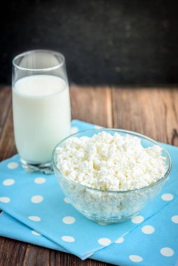 Koyu ahşap masada süzme peynir ve bir bardak süt.