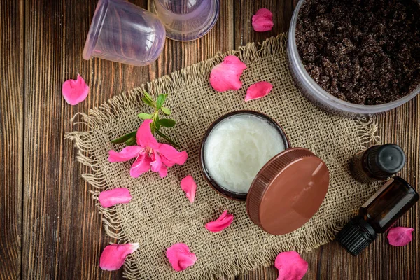 Coffee body scrub, sugar and coconut oil, essential oils, massage vacuum jars on dark wooden rustic table with pink flowers.