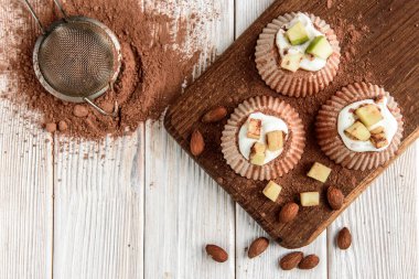 Beyaz ahşap arka planda kakao, elma ve badem ile ev yapımı çikolatalı süzme peynir suflesi..
