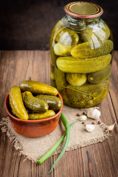 Pickled cucumbers in bowl on wooden rustic table with garlic and jar of pickles.