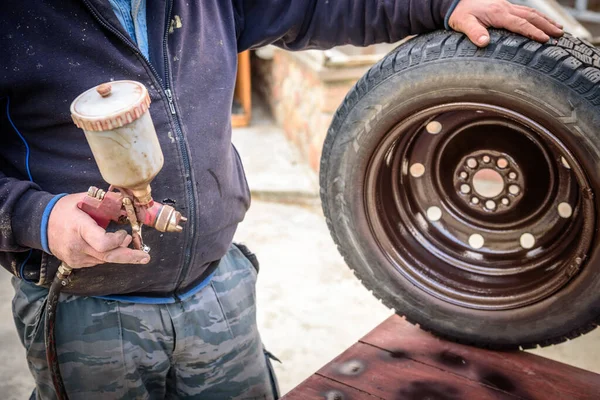 Man paints sprayer car disk with using spray gun.