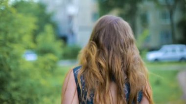 Genç kadının Caddesi yakınlarında ağaç yürürken arkadan görünüm. Rüzgarda sallayarak saç. Kız arkasını döner. Yavaş mo.