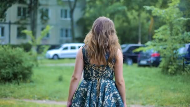Вид сзади на молодую женщину, идущую по улице рядом с деревом. Волосы машут на ветру. Девушка поворачивается. Медленно . — стоковое видео