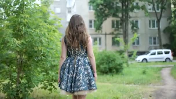 Vista posteriore della giovane donna bruna che cammina per la strada vicino all'albero. Capelli agitati dal vento. La ragazza si gira. . — Video Stock