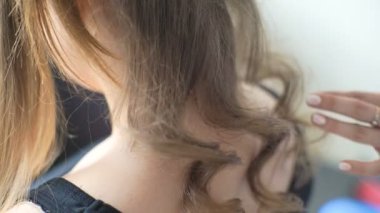 Kuaför, güzel bir kızın dikiz aynasındaki saç modelinin son aşamasını oluşturuyor. Profesyonel kuaför, sevimli Avrupalı küçük bir kız için saç stili yapıyor..