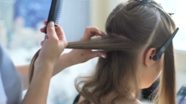 Волосач робить фінальний етап створення зачіски для милої дівчини, заднього виду. Професійний стиліст перукаря робить зачіску для милої європейської маленької дівчинки в будинку.. — стокове відео