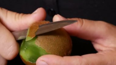Kadın bir ısırık almak için kivi soyar.