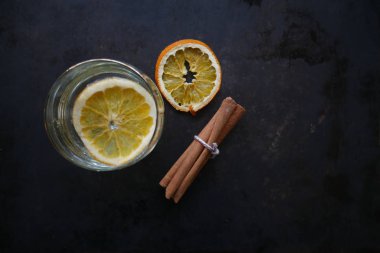 Bir cam, turuncu bir dilim ve Kuru portakal dilimleri ve tarçın karanlık bir arka plan üzerinde bir dizi