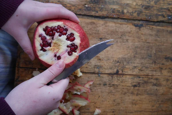 Man cuts a ripe pomegranate with a knife on  wooden background — Stock Photo, Image