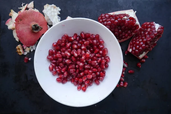 white plate with pomegranate fruit next to pomegranate pieces and pomegranate peel on a dark background