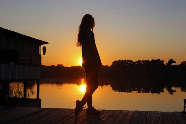 Lány sziluettje egy híd, a tó naplementekor — Stock Fotó