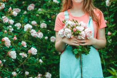 Bahçeden taze gül buketi toplayan genç bir kadın.