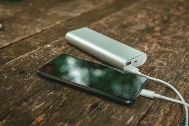 Tahta arka planda elektrik bankası olan boş batarya akıllı telefonunu şarj etmek 