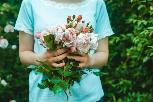 Genç bir kadın çiçekçi elinde pembe güllerden bir buket tutuyor. Bahçede