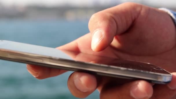 Close up disparo de mans manos con teléfono móvil a la vista de mar de fondo — Vídeos de Stock