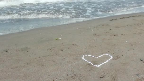 Αφρώδη κύμα που πλένει πέρα από πέτρα βότσαλο καρδιά στην άμμο — Αρχείο Βίντεο