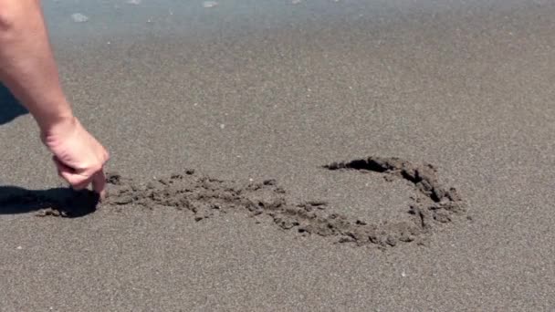 Młody człowiek writte serca na piaszczystej plaży — Wideo stockowe