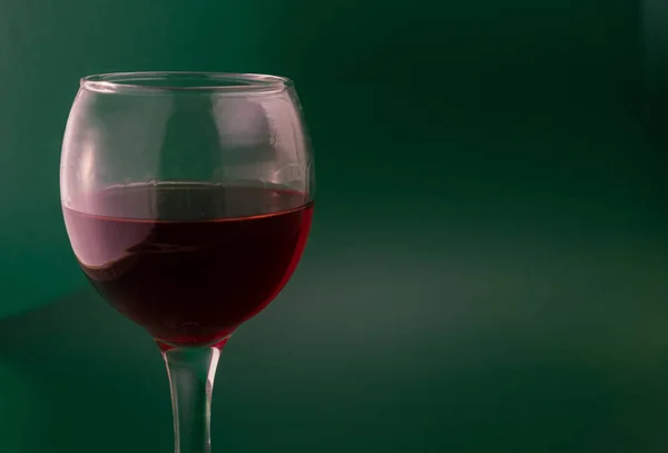 A glass of red grape wine on a green background