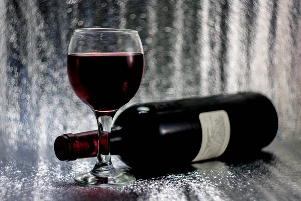 Bir bardak kırmızı üzüm şarap, bir şişe şarap simli bulanık bokeh arka plan üzerinde