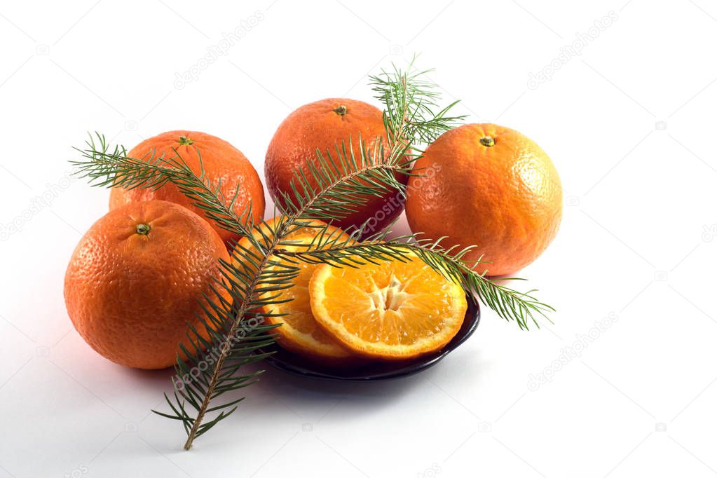  Tangerines whole and cut in a black plate on a white background with a branch of spruce