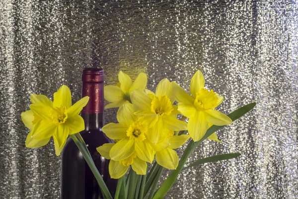Early spring flowers and a bottle of red grape wine on a silver background
