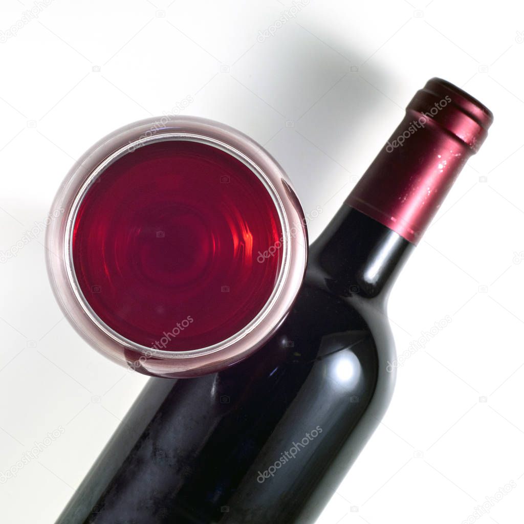 A bottle of red wine with a glass. Square image. View from above.
