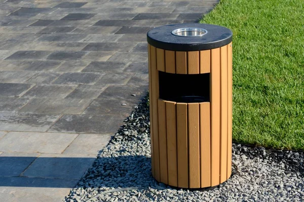 Trash can on the street in the park near the stone road and grass. Clean bin