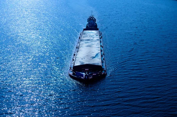 The towed barge floats on the water, the photo in cold tones. Barge with sand on the sea, river, lake or port. Minimalistic photo