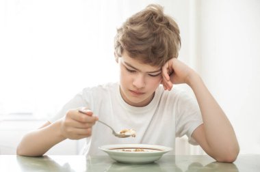 Çocuk bir tabak yulaf lapasının önünde masada oturur. Yemek yemek istemiyor..