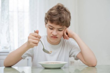 Çocuk bir tabak yulaf lapasının önünde masada oturur. Yemek yemek istemiyor..