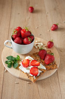 Çilekli ve krem peynirli hafif kahvaltı. Ahşap bir arka planda ve yuvarlak ahşap bir stantta kırsal tarzda. Dikey fotoğraf.