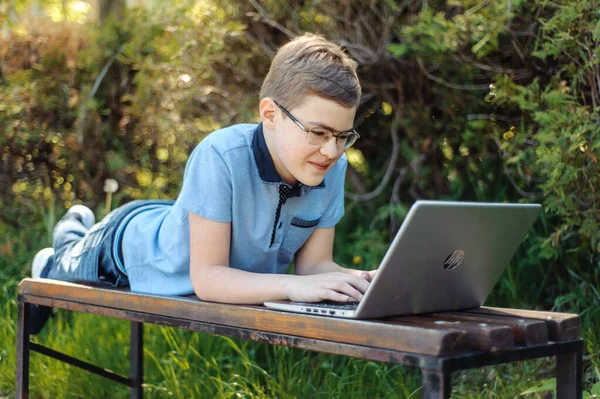 少年は遠隔で学ぶ 公園にノートパソコンを持った10代 彼の距離を保って あの少年はベンチに一人でいる — ストック写真