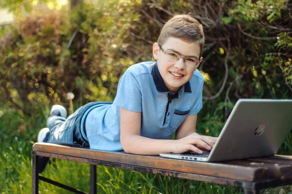 少年は遠隔で学ぶ 公園にノートパソコンを持った10代 彼の距離を保って 少年はベンチに一人でいる カメラを見てみろ — ストック写真