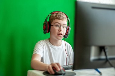 Kulaklığı ve mikrofonu olan bir çocuk bilgisayar monitörünün önünde..