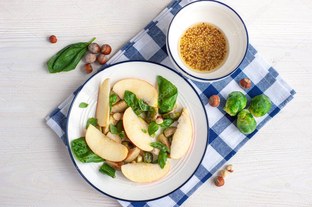Brussels sprouts, apples and basil salad on a light background with a checkered napkin.