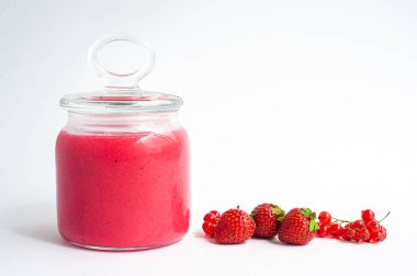 Cam kavanozda kırmızı üzümlü çilek reçeli ve beyaz arka planda kapağı var..